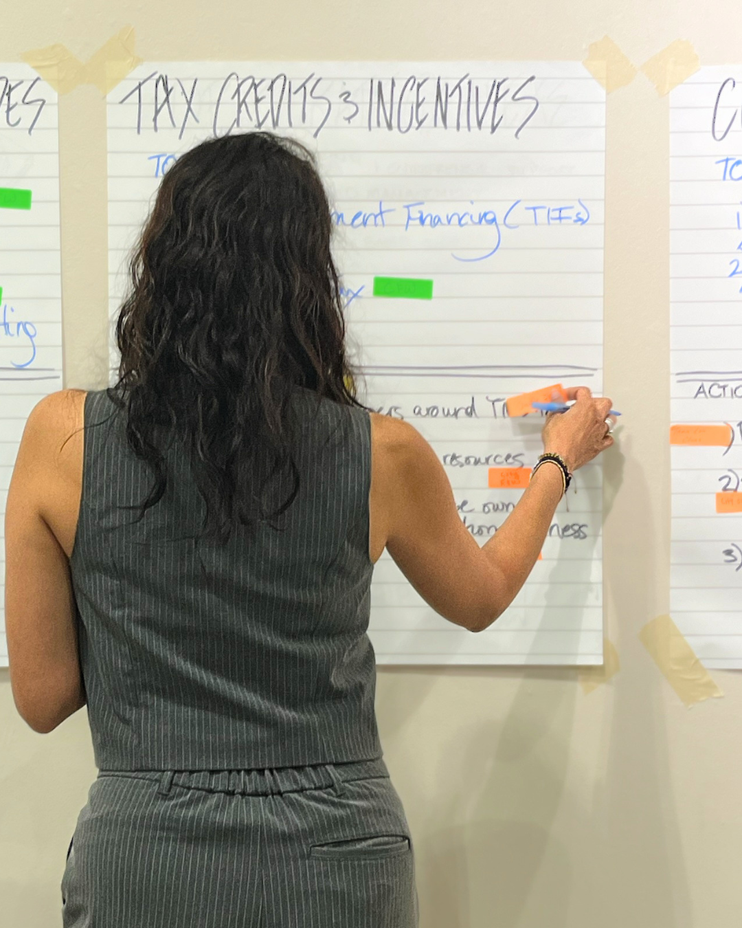 a workshop participant adds her sticky-note suggestion to a large piece of paper taped to the wall which reads "tax credits and incentives."